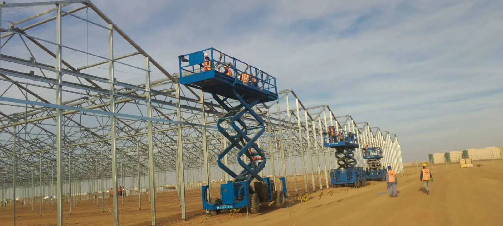 Workers on lifts installing a shade house frame