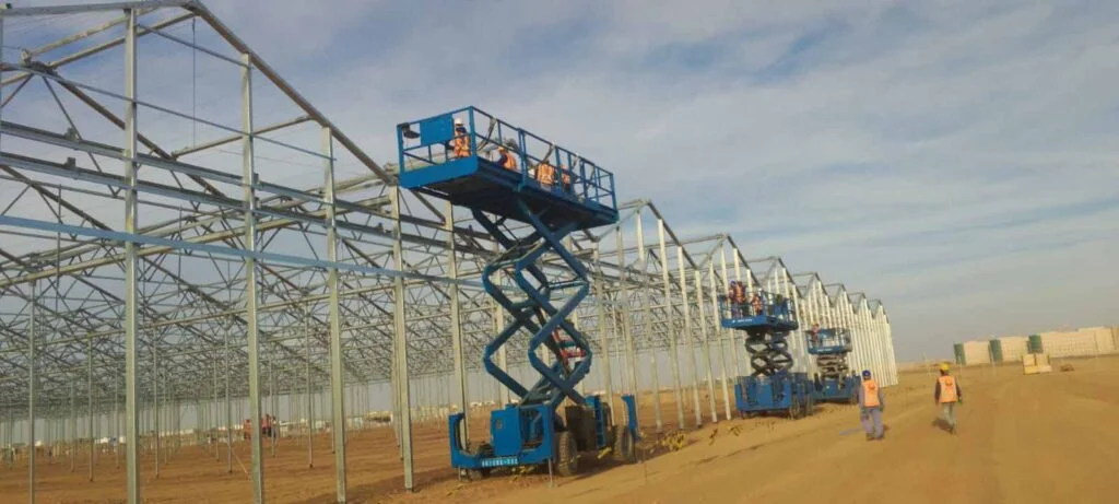 Crews on lifts assembling a large greenhouse steel frame